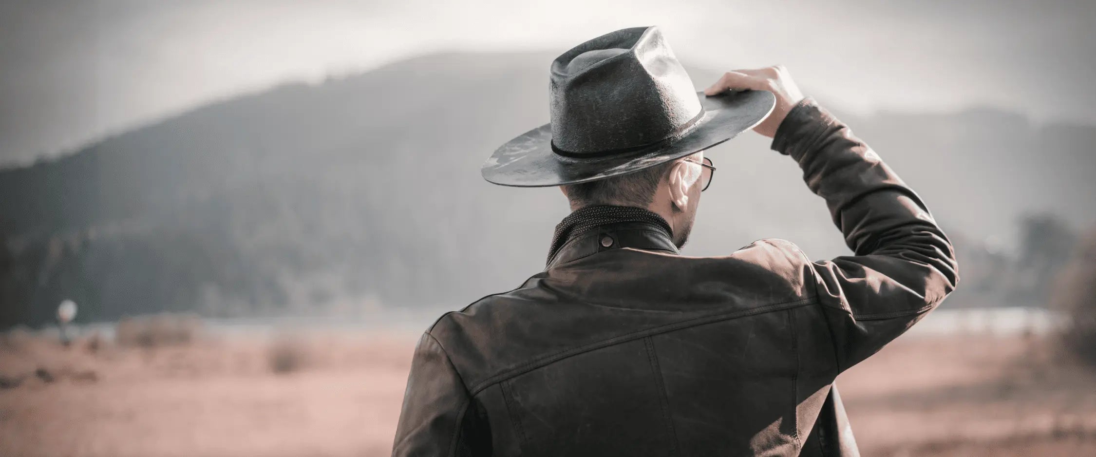 Man in a leather jacket and hat looking out over a desert landscape