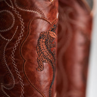 Close-up of a brown leather product with intricate stitching and a tiger design.