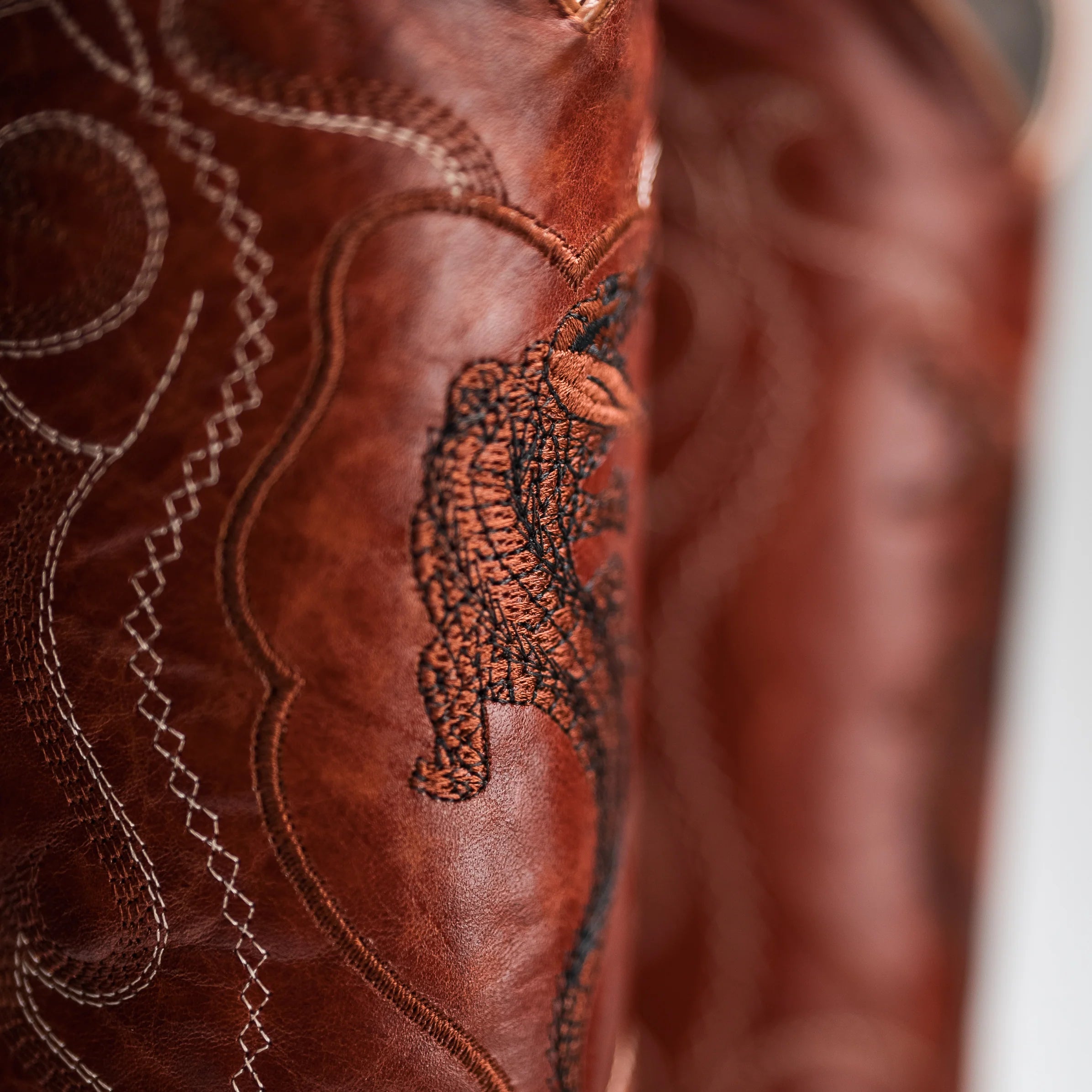 Close-up of a brown leather product with intricate stitching and a tiger design.