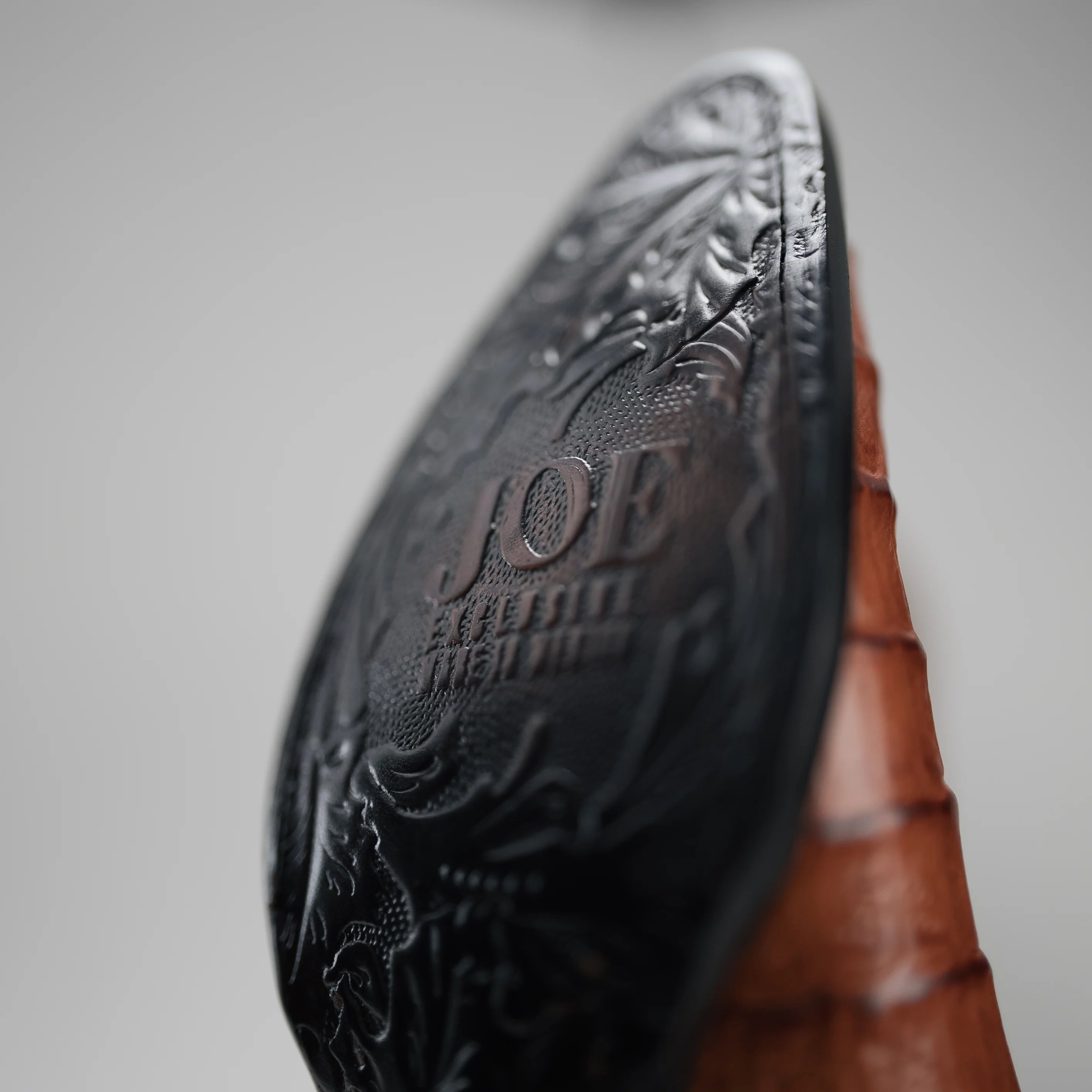 Close-up of a brown leather boot with embossed design and 'JOE' branding on a gray background
