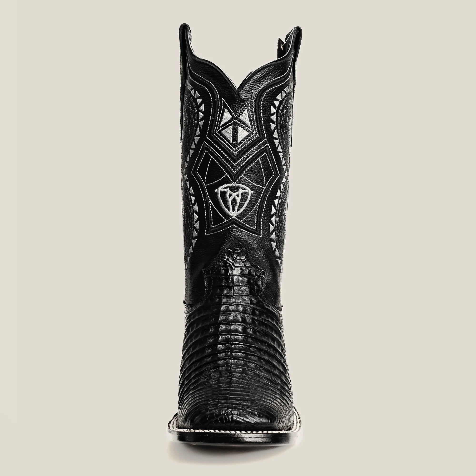 Black cowboy boot with intricate design on a beige background