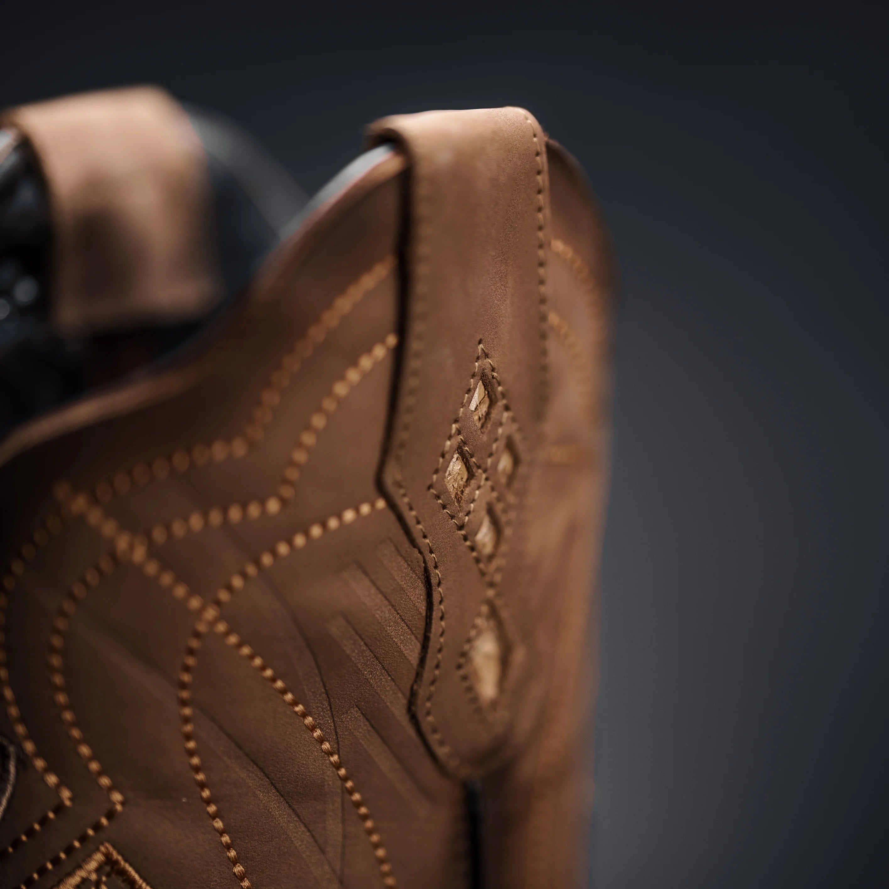 Close-up of a brown leather boot with intricate stitching on a dark background