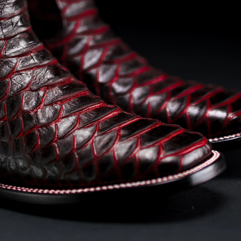 Close-up of black leather boots with red stitching on a dark background