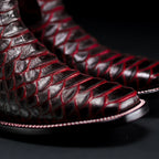 Close-up of black leather boots with red stitching on a dark background