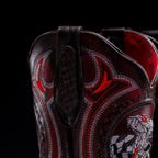 Close-up of a dark brown leather bag with red and black embroidery on a black background