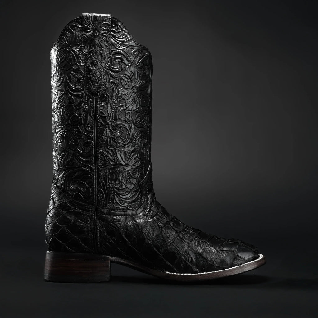 Black leather cowboy boot with intricate embossing on a dark background
