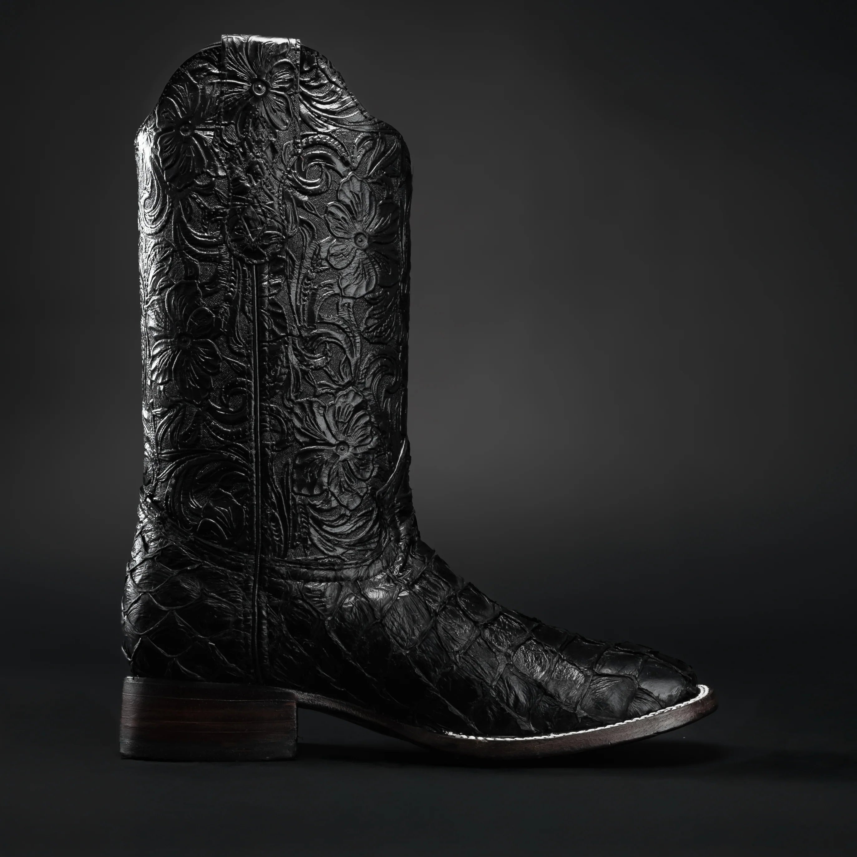 Black leather cowboy boot with intricate embossing on a dark background