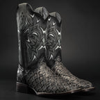 Black cowboy boot with intricate white embroidery on a dark background