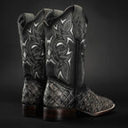Pair of black and silver cowboy boots with intricate designs on a dark background