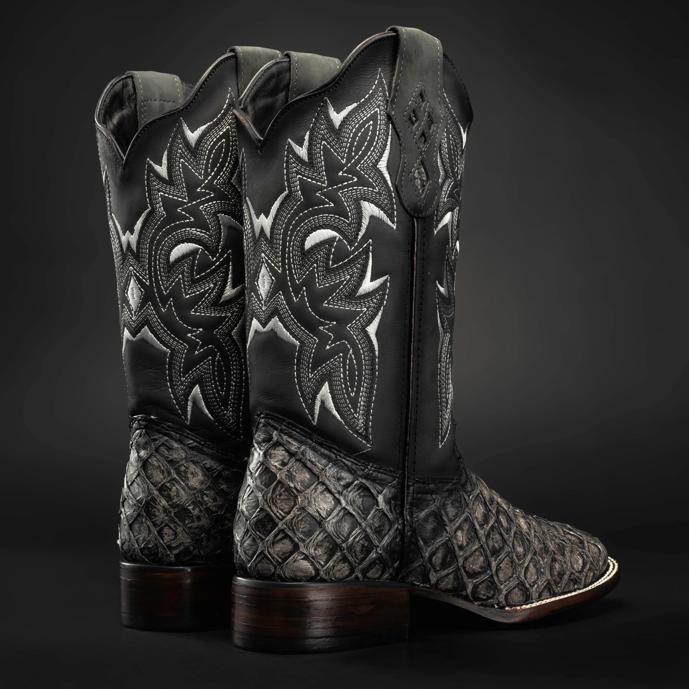 Pair of black and silver cowboy boots with intricate designs on a dark background