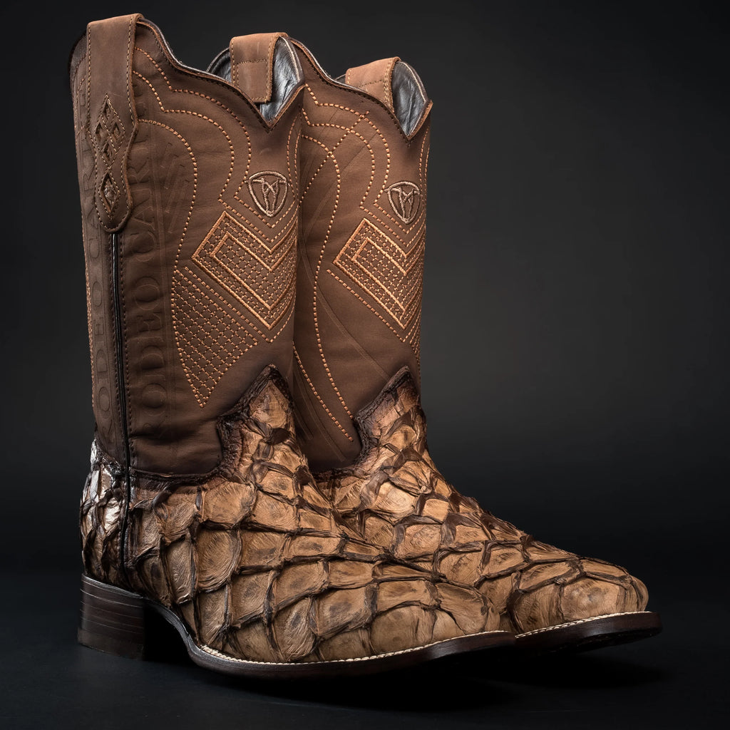 Brown cowboy boots with patterned soles on a black background