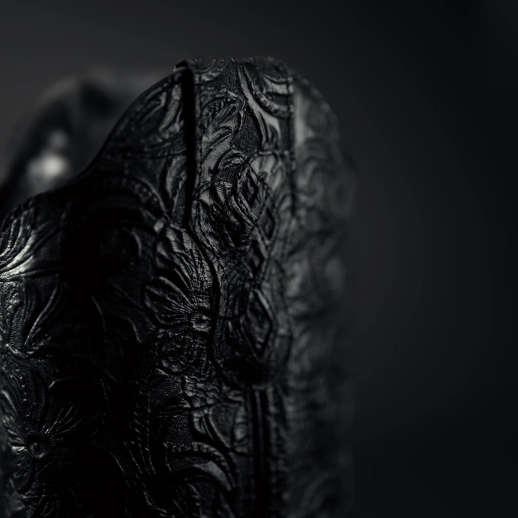 Close-up of a black embossed coy boy bo0ts on a dark background