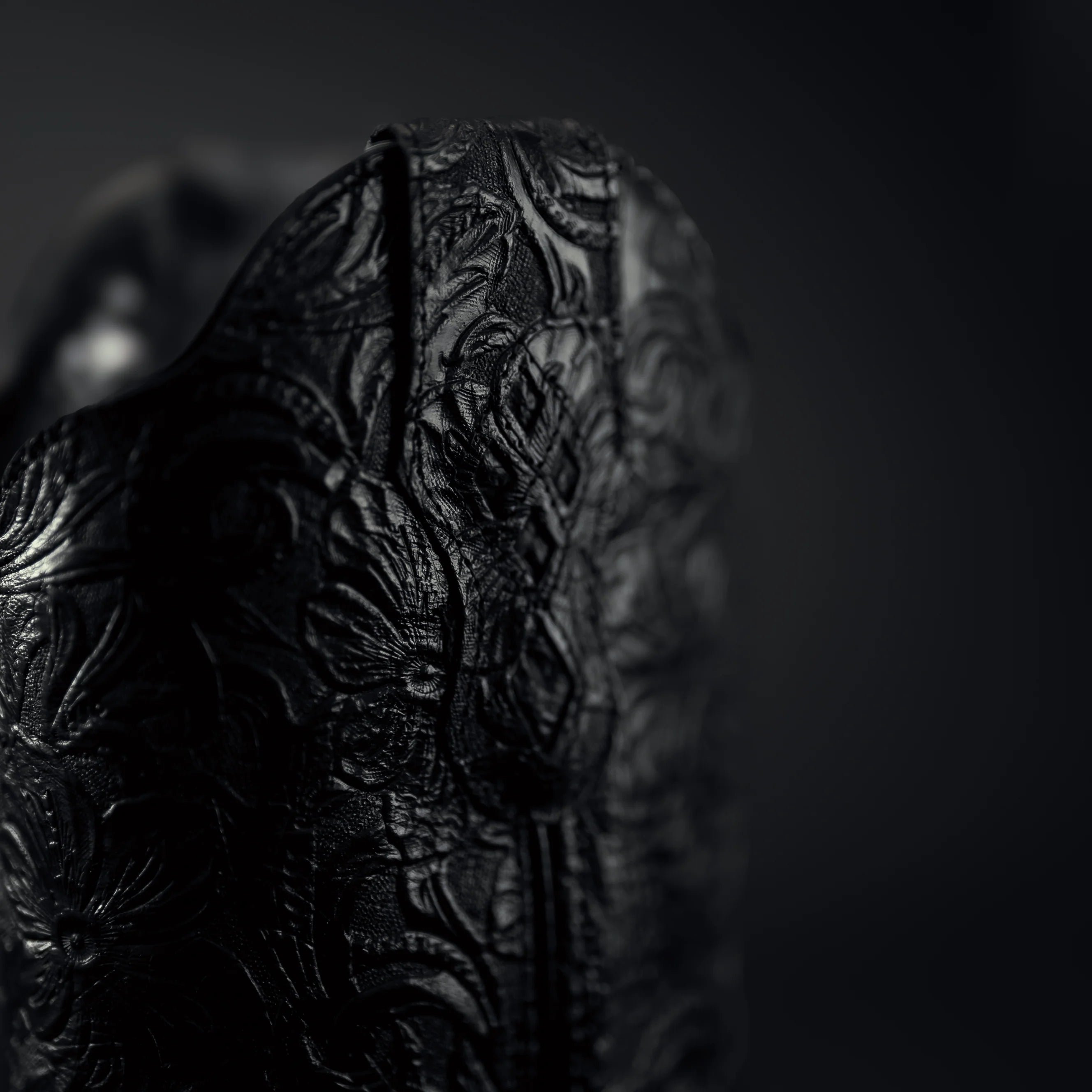 Close-up of a black embossed coy boy bo0ts on a dark background