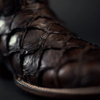 Close-up of a brown leather boot with detailed stitching on a dark background