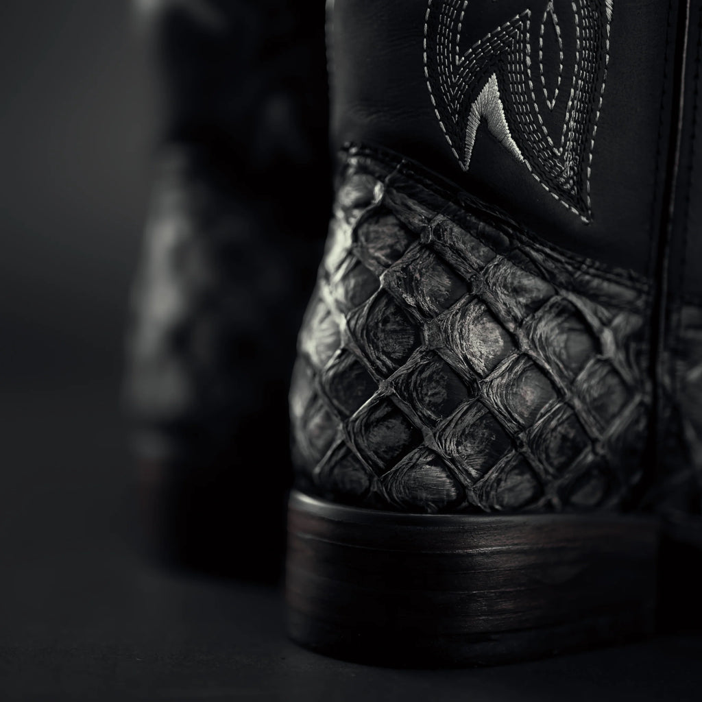Close-up of a black leather boot with detailed stitching on a dark background