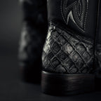 Close-up of a black leather boot with detailed stitching on a dark background