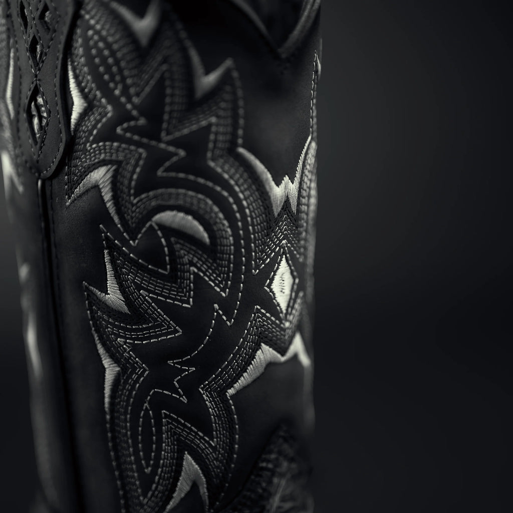 Close-up of a black leather product with intricate white embroidery on a dark background